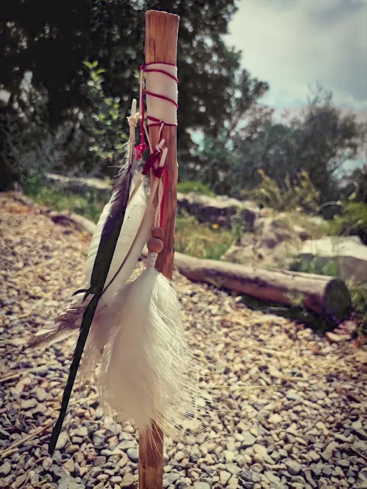 Un bâton orné de plumes et de rubans planté dans la terre, en pleine nature.