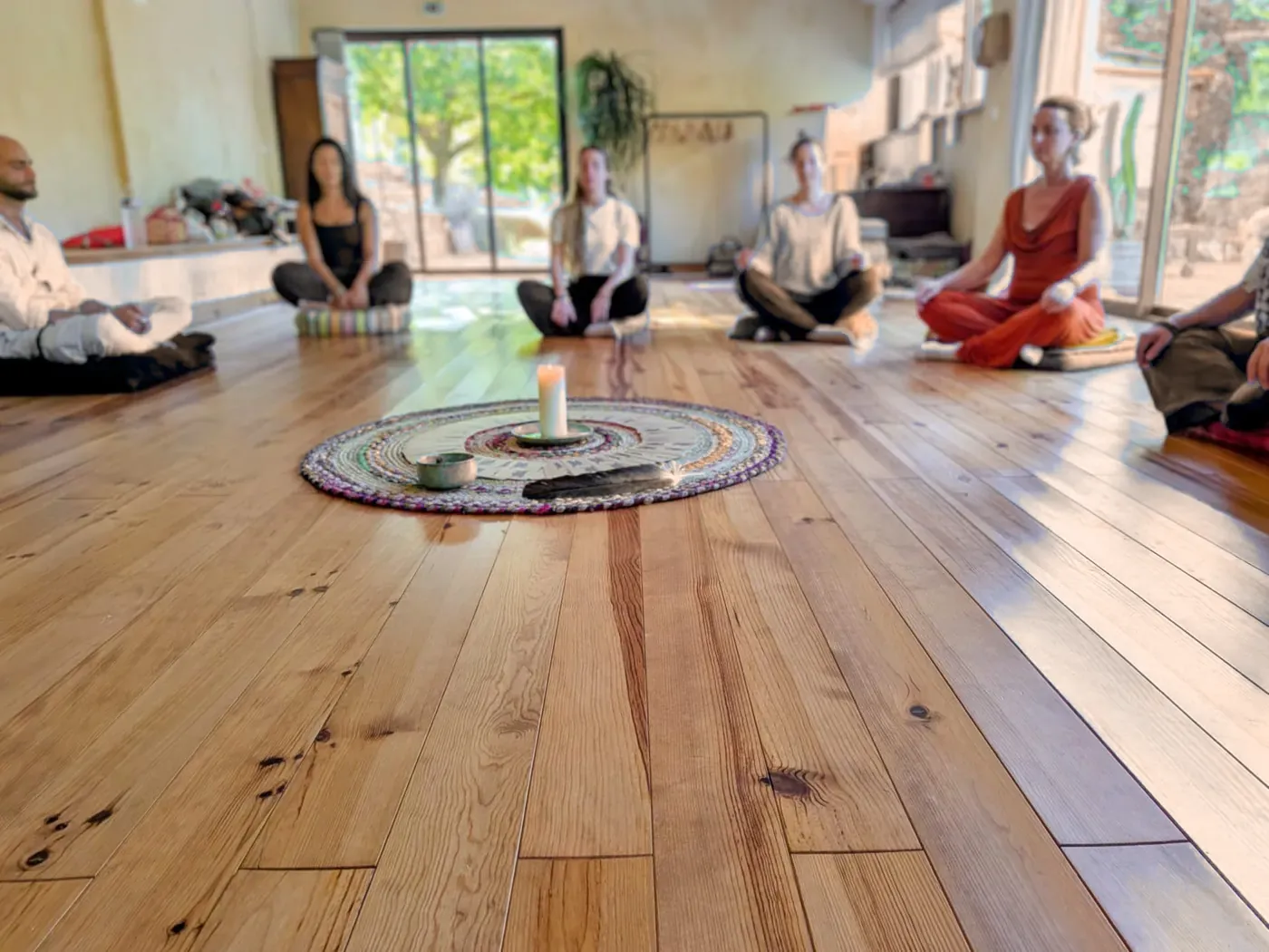 Un groupe assis en cercle sur un parquet, autour d'un mandala et d'une bougie.