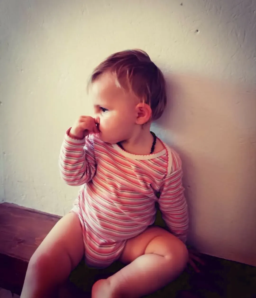 Un tout-petit assis contre un mur, l'air pensif, un doigt sur le nez.