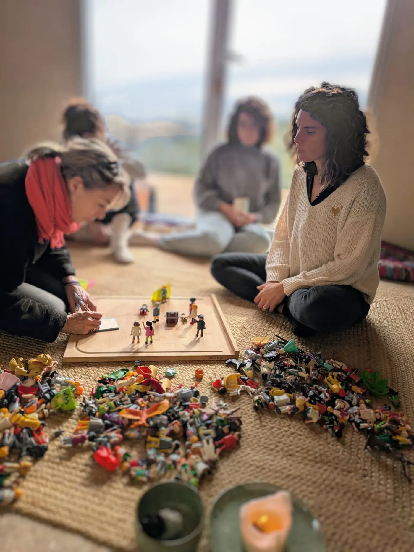 Sandrine assise au sol avec deux participantes autour d'un plateau de figurines Playmobil.
