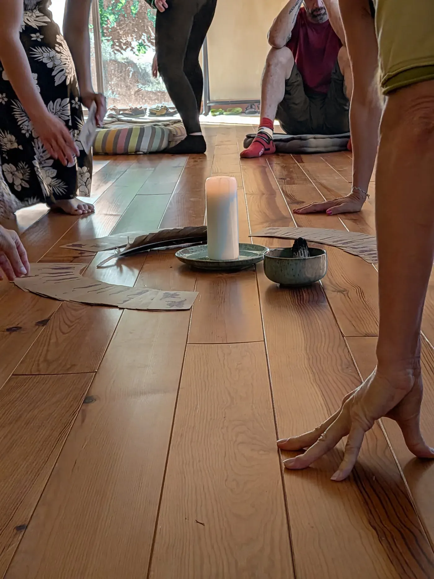 Des participants debout autour d'une bougie et de cartes posées sur le parquet.