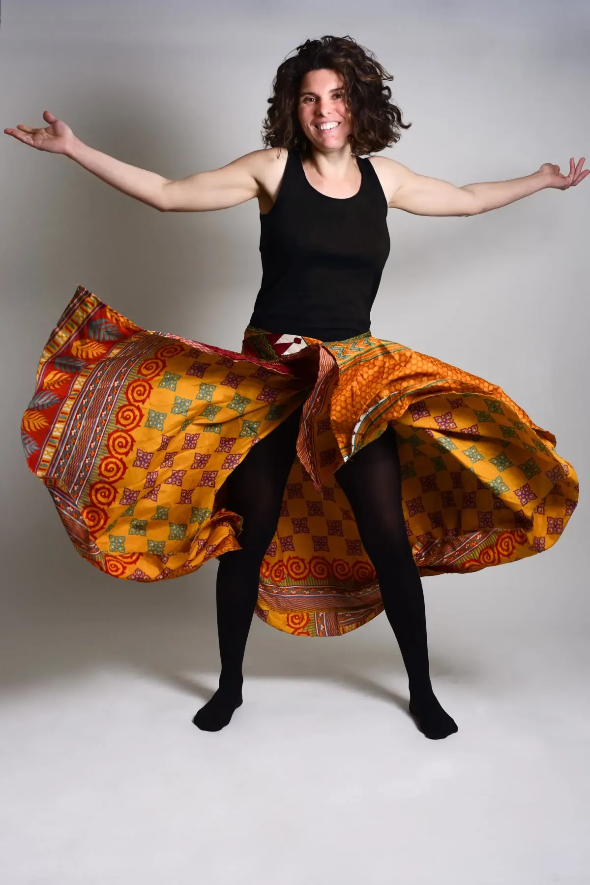Sandrine qui danse, les bras ouverts, dans une jupe aux motifs orange et or.