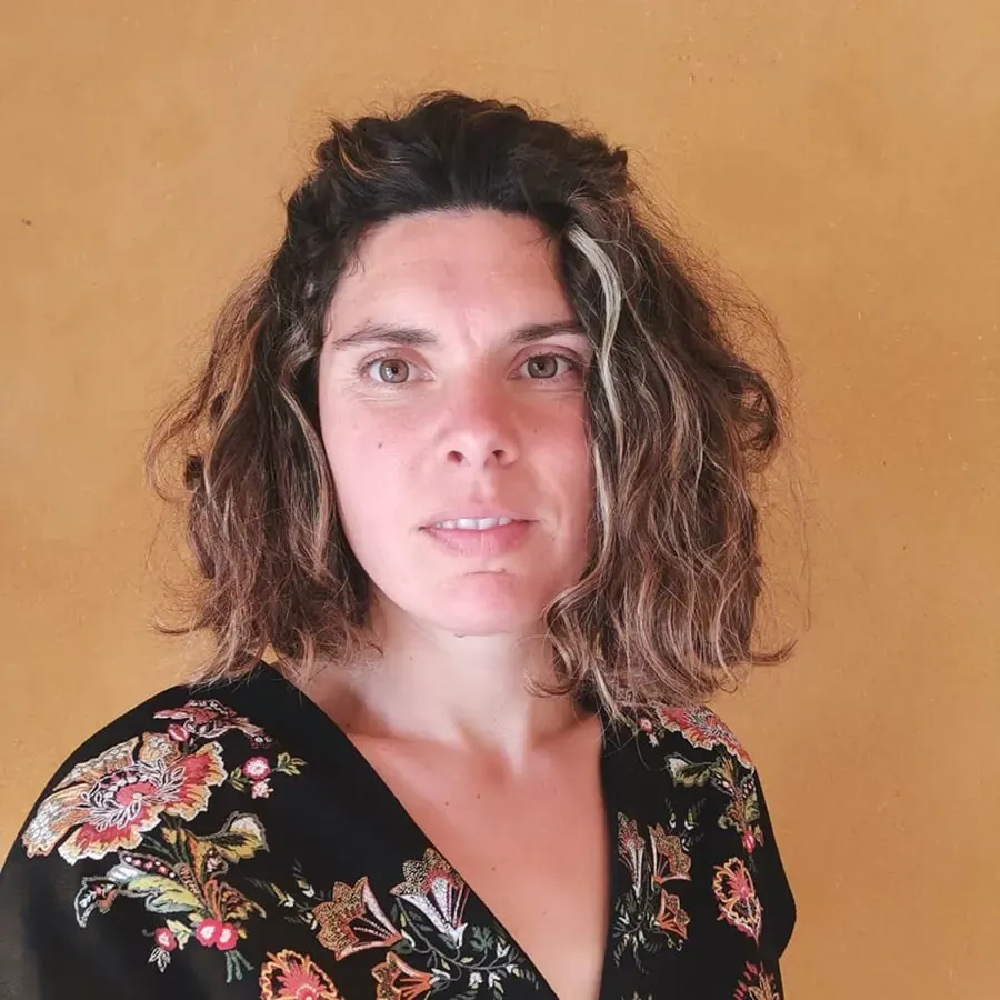 Portrait de Sandrine, cheveux bouclés, devant un mur ocre.