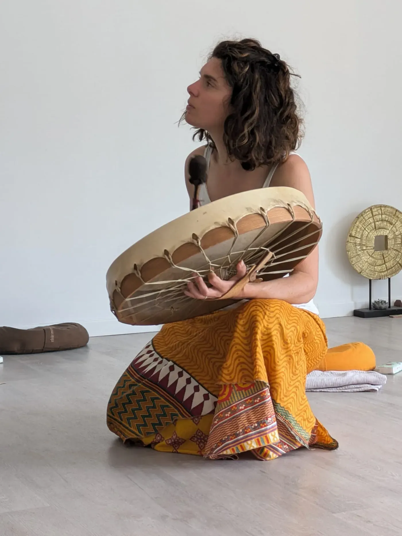 Sandrine à genoux, son tambour entre les mains, le regard levé.