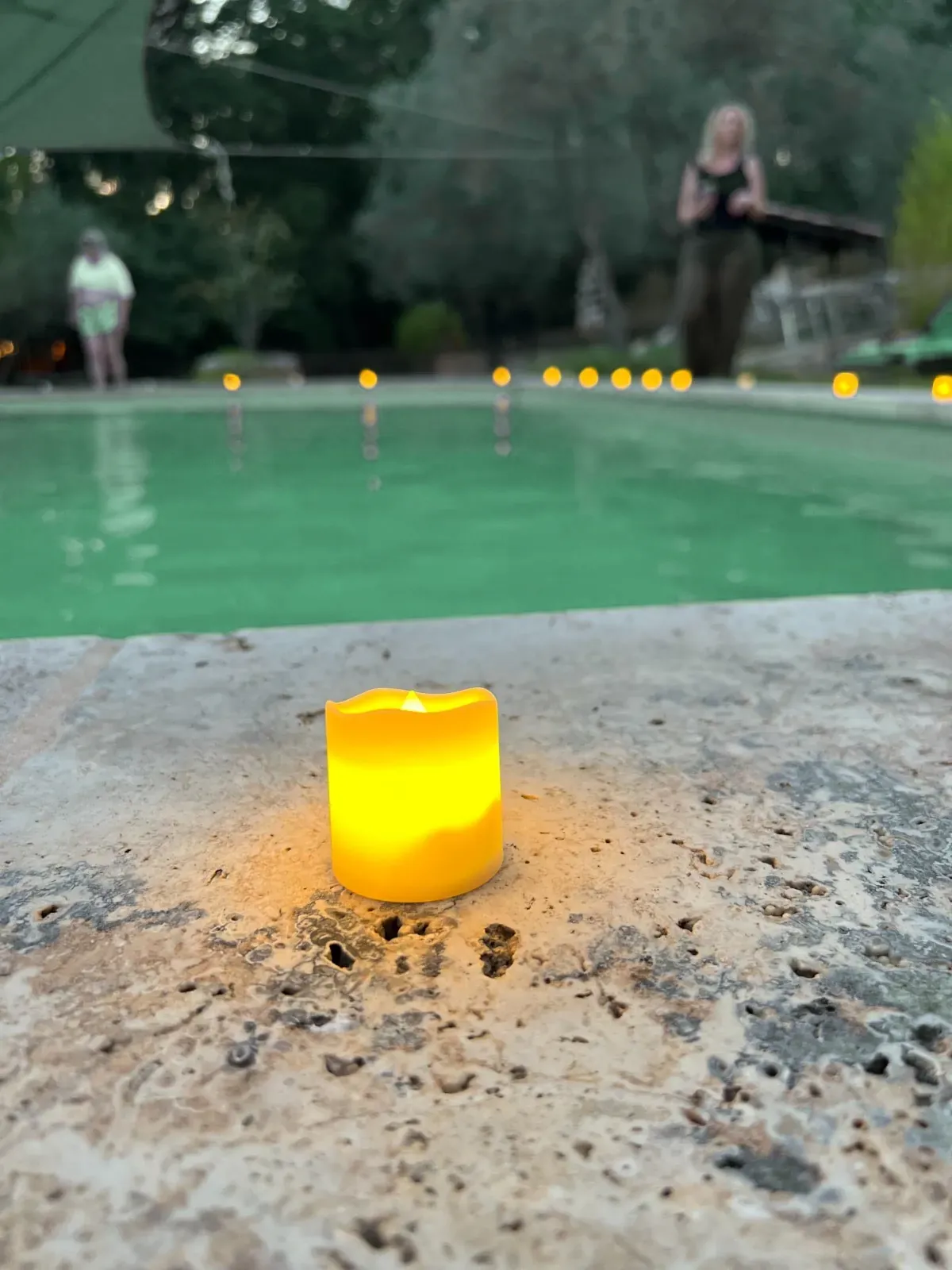 Une bougie allumée au bord d'un bassin, à la tombée de la nuit.