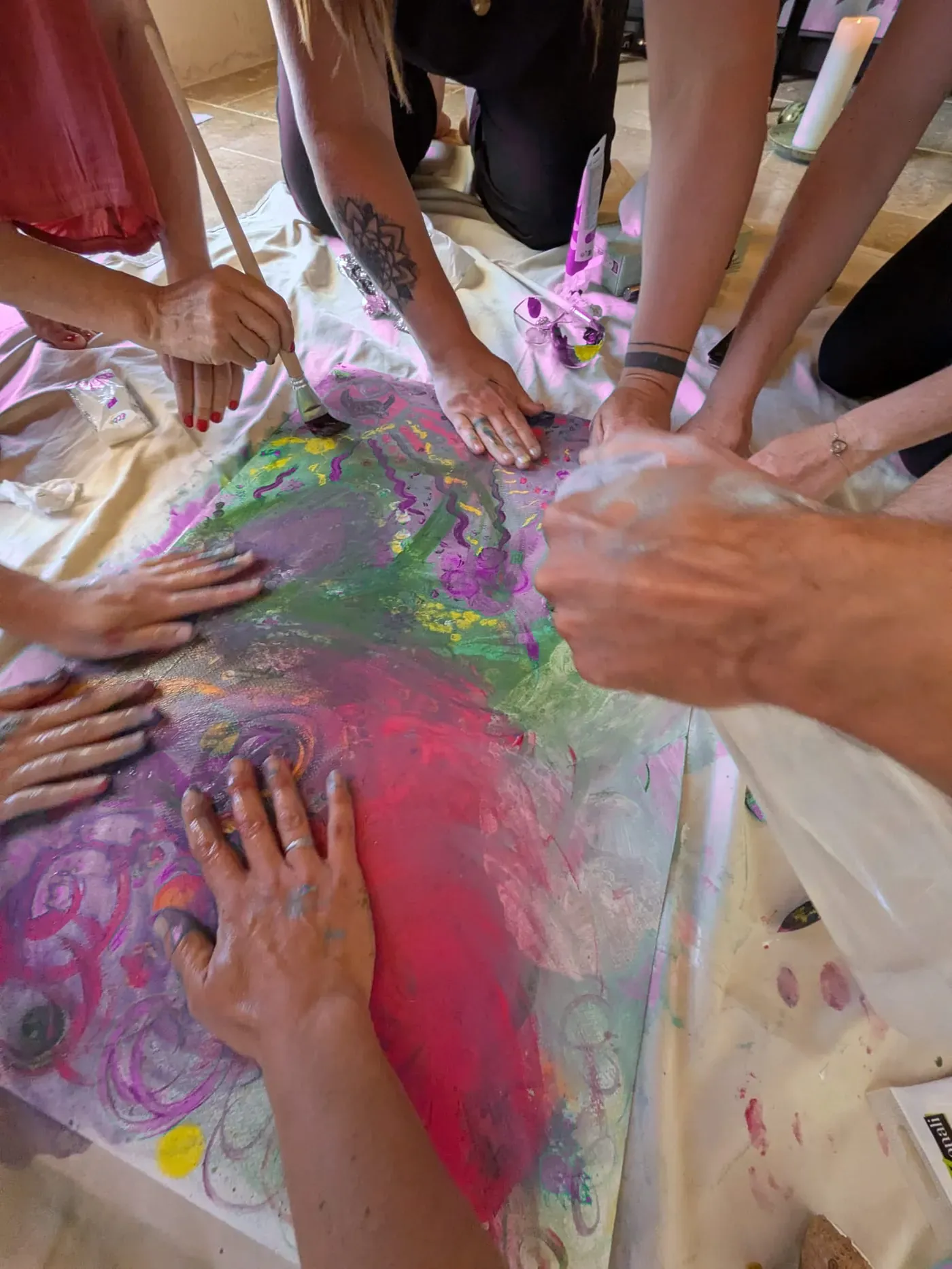 Des mains peignent ensemble une grande toile colorée posée au sol.